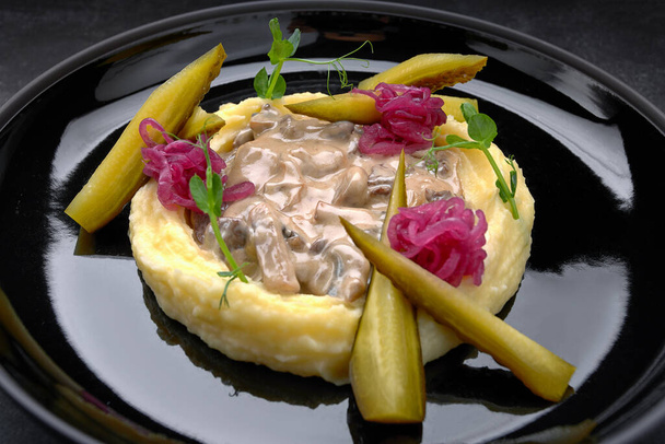 Purè di patate con funghi in salsa e cetrioli sottaceti, su uno sfondo scuro - Foto, immagini