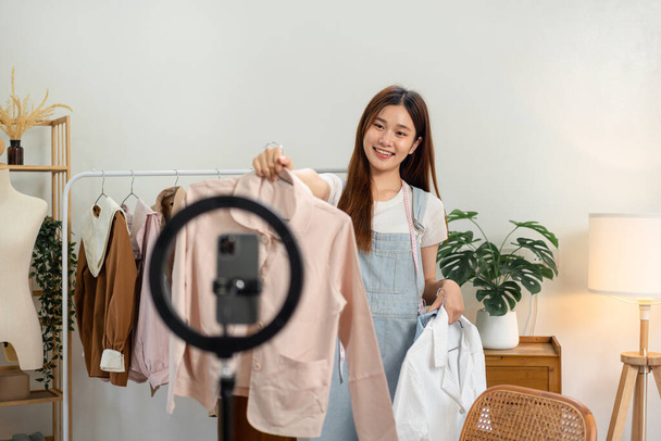 Online-Verkäuferin nutzt Smartphone, um live auf Vlog Mode vorzustellen, während sie Hemd zur Präsentation der neuen Kollektion zeigt und Online-Kleidung in den sozialen Medien verkauft. - Foto, Bild