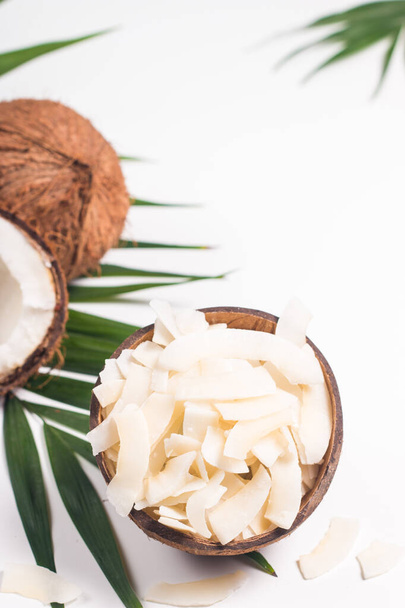 Chipsy kokosowe z kokosem i zielonymi liśćmi na białym tle. Koncepcja izolowana. - Zdjęcie, obraz