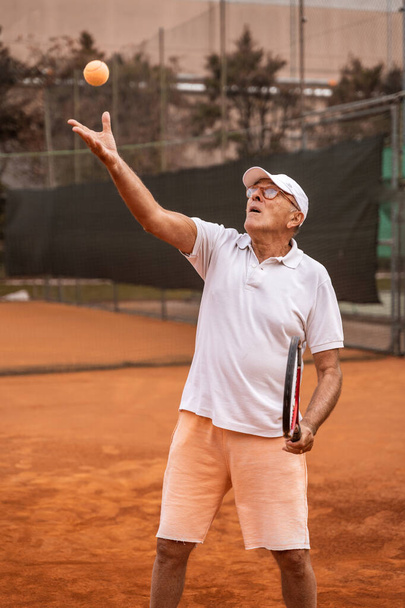 Senior tenista oblečený do sportovního oblečení v akci na hliněném tenisovém kurtu - penzion wellness koncept - Fotografie, Obrázek