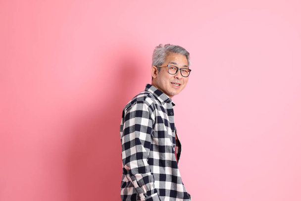 40代のアジア系男性がピンクの背景にカジュアルな服で立っています. - 写真・画像