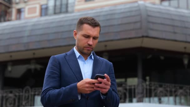 Porträt eines gutaussehenden kaukasischen Mannes, der mit dem Smartphone durch die Stadt läuft. Junge erfolgreiche Gentleman SMS online auf dem Handy. Technologie, Kommunikationskonzept. Geschäftsstädtisches - Filmmaterial, Video