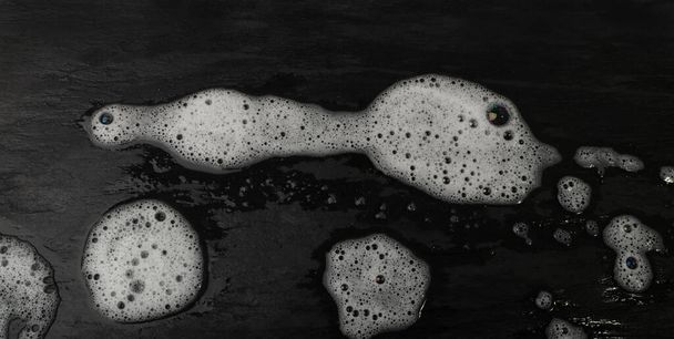 Detergent foam texture background. Lather pattern, soap bubbles on black stone surface, soap foam wallpaper with copy space - Foto, Imagem
