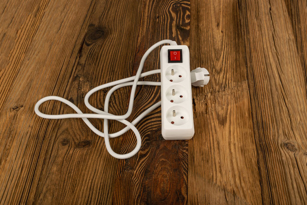 Полоса питания на деревянном фоне. Удлинитель кабеля, электрическая полоса, розетка, белый удлинитель мощности, удлинитель на деревянных полах - Фото, изображение