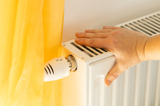 La mano di una donna controlla se il radiatore sta riscaldando, Costi di riscaldamento della casa e degli appartamenti, Aumento dei prezzi dell'energia, Paure dell'inverno e del freddo, interruzioni di corrente - Foto, immagini