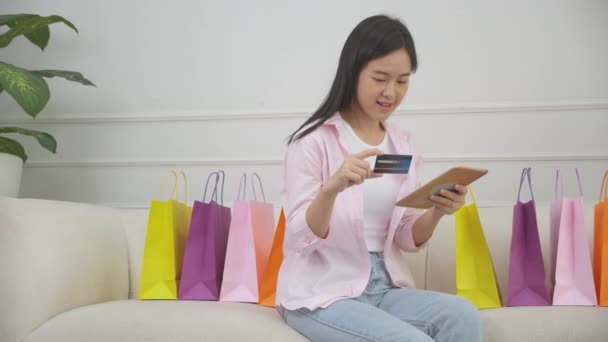 Young asian woman sitting on sofa using digital tablet shopping online with credit card buying to internet, happiness girl paying with transaction financial, purchase and payment, business concept. - Footage, Video