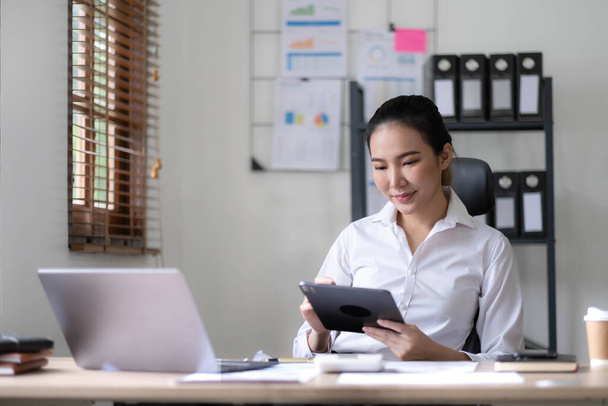 Photo of cheerful young woman working using tablet concentrated and smiling at office.. - Photo, Image