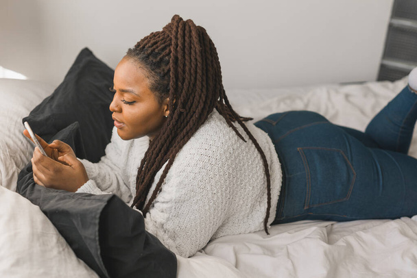 Retrato de uma estudante africana bonita vestida casualmente segurando telefone celular e digitando mensagens e se comunicando com amigos redes sociais usando conexão de alta Internet. - Foto, Imagem