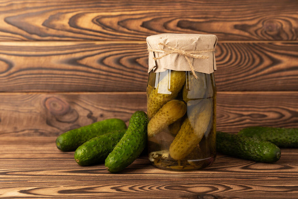 A jar of pickles. Canned cucumbers in a jar on a brown wooden background. Collection of vegetables. Pickled jars. Stocks for the winter. home preservation. pickles. Copy space - Photo, Image