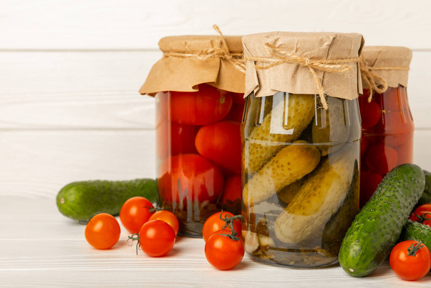 Potten met gepekelde groenten. Ingelegde voeding.Potten met ingemaakte groenten: komkommers en tomaten op een rustieke houten ondergrond. Ingeblikt en conserven. - Foto, afbeelding