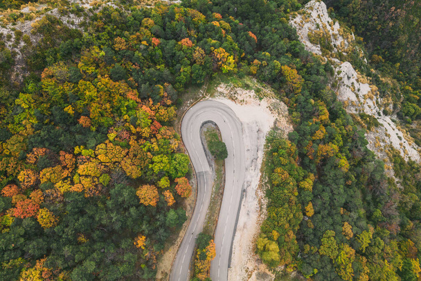 高い山からの曲がりくねった道の空中ビューは、密なカラフルな秋の森を通過します。. - 写真・画像