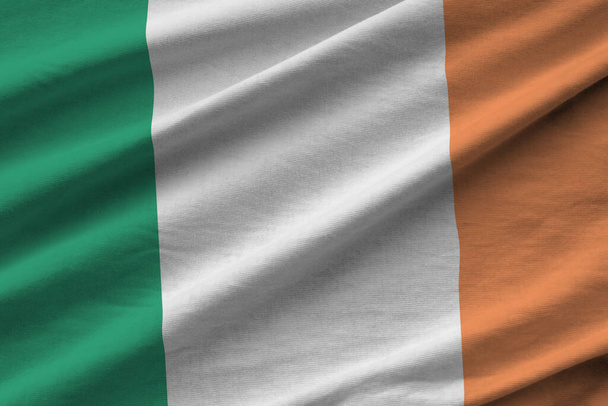 Irland-Flagge mit großen Falten, die aus nächster Nähe unter dem Studiolicht im Innenraum weht. Die offiziellen Symbole und Farben in Stoffbanner - Foto, Bild