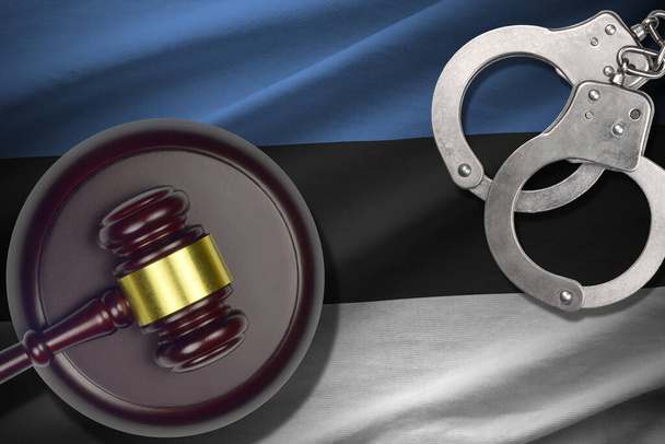 Estland vlag met rechter hamer en handboeien in donkere kamer. Concept van strafbaarheid en bestraffing, achtergrond voor schuldige onderwerpen - Foto, afbeelding