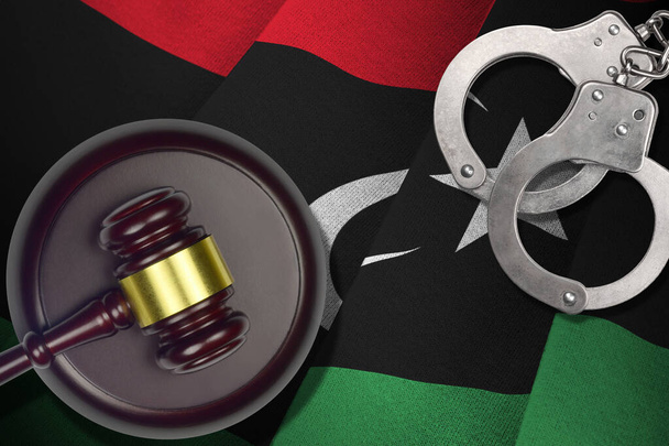 Libië vlag met rechter hamer en handboeien in donkere kamer. Concept van strafbaarheid en bestraffing, achtergrond voor schuldige onderwerpen - Foto, afbeelding