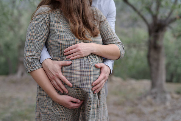 Een zwangere vrouw en haar man houdt haar buik vast met liefdevolle handen. - Foto, afbeelding