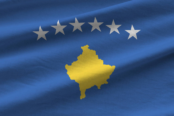 Bandera de Kosovo con grandes pliegues ondeando de cerca bajo la luz del estudio en el interior. Los símbolos oficiales y los colores en banner de tela - Foto, Imagen
