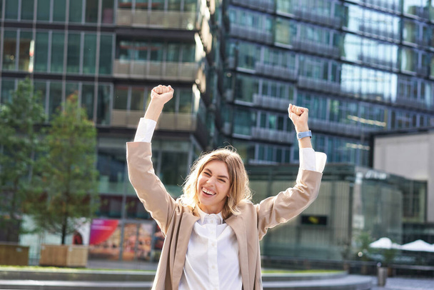 Corporate woman celebrating her victory outside on street. Happy businesswoman raising hands up and triumphing from excitement. - Photo, Image