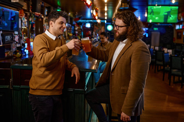 パブでビールマグカップでクリンクして幸せな男性の友人。楽しい若者たちが一緒にいる。友情の概念 - 写真・画像