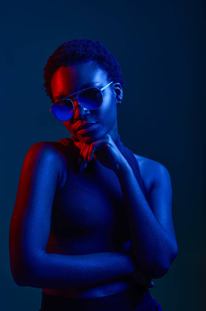 Pensive woman in sunglasses over dark studio background with copy space and neon light - Valokuva, kuva