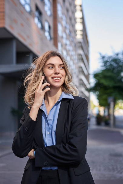 Colpo verticale di giovane donna d'affari fiduciosa che fa una telefonata, in piedi sulla strada e parla al telefono. - Foto, immagini