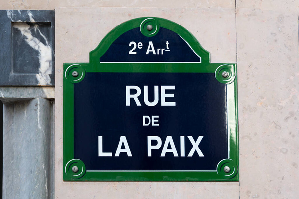 Paris, Fransa 'da Place de l' Opera 'yı Place Vendome' a bağlayan bir sokak, üzerinde "Rue de la Paix" ("Barış Sokağı" anlamına gelen) yazan geleneksel Paris sokak tabelası. "Rue de la Paix" Monopoly 'nin Fransızca baskısının en pahalı caddesi. - Fotoğraf, Görsel
