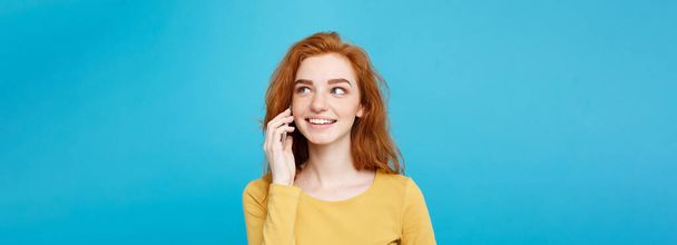 Lifestyle- und Technologiekonzept - Portrait eines fröhlichen, rothaarigen Mädchens mit fröhlichem und aufregendem Gespräch mit einem Freund per Handy. isoliert auf blauem Pastellgrund. Kopierraum - Foto, Bild
