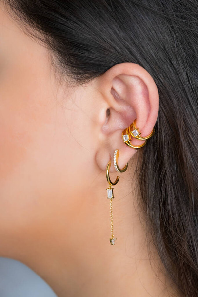 Жіноче вухо з різноманітними пірсингами в красивих сережках з цирконією- деталями захоплення. Прекрасний подарунок валентина
. - Фото, зображення