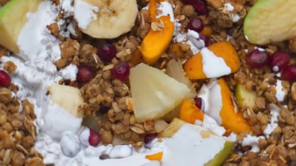 Sweet sliced fruits with cereals poured with fresh organic milk close up. Vitamin nutrient muesli with juicy pineapple apricot banana pomegranate apple preparing with white yogurt. Healthy food. - Footage, Video