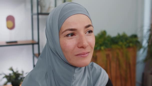 Портрет счастливой спокойной молодой мусульманской деловой женщины в хиджабе, улыбающейся дружелюбно, с приятным выражением лица, мечтательным отдыхом, релаксацией - приятная новость. Девушка в современном домашнем офисе - Кадры, видео