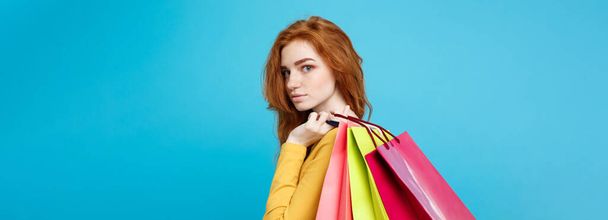 ショッピングのコンセプト - クローズ アップ肖像若い美しい魅力的な redhair 女の子のカメラ目線します。青いパステル背景。コピー スペース - 写真・画像