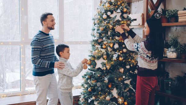 Parents and kid are decorating New Year tree in modern apartment talking having fun together. Beautiful interior, people and holidays concept. - Fotoğraf, Görsel