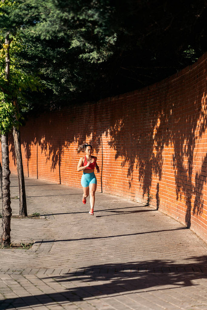 Strong asian woman with sports clothes working out in the street during sunny day. She is running and looking at front. - Fotoğraf, Görsel