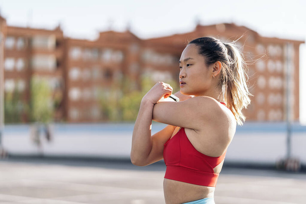 Young chinese woman wearing sports clothes looking at front and stretching her arms after her workout. - Fotografie, Obrázek