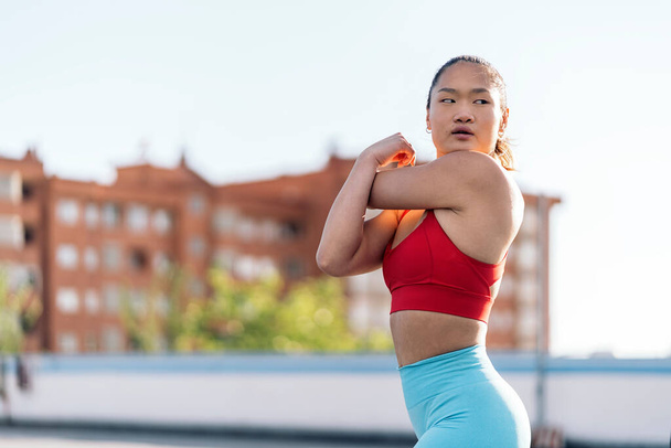 Young chinese woman wearing sports clothes looking to the side and stretching her arms after her workout. - Φωτογραφία, εικόνα