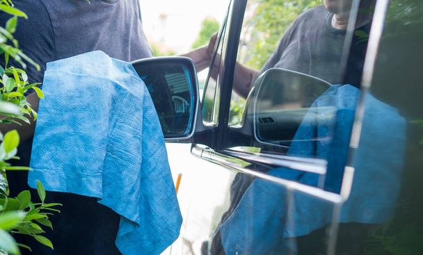 Die Hand eines Mannes reinigt den Seitenspiegel des Autos mit einem blauen Mikrofasertuch. - Foto, Bild