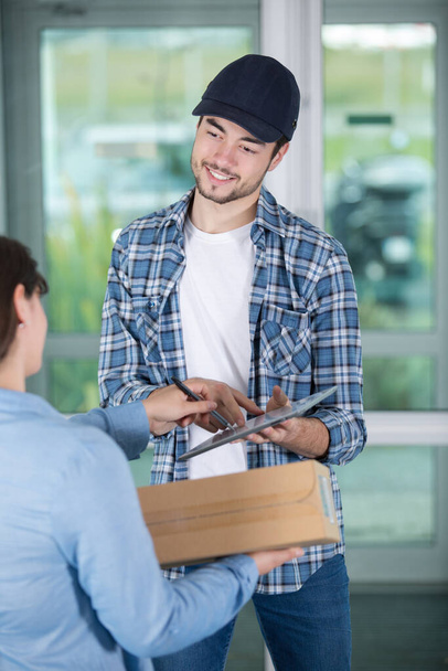smiling young delivery man holding a clipboard - Foto, Bild