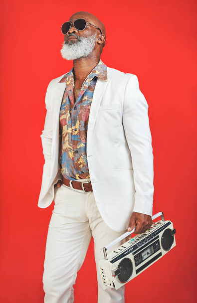 Show me someone cooler than me. Studio shot of a senior man wearing vintage clothing while posing with a boombox against a red background - Foto, Imagem