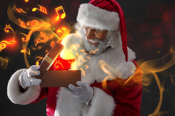 Noel Baba 'yla kolaj, karanlık arka planda hediye kutusu ve nota işaretleri açıyor. - Fotoğraf, Görsel