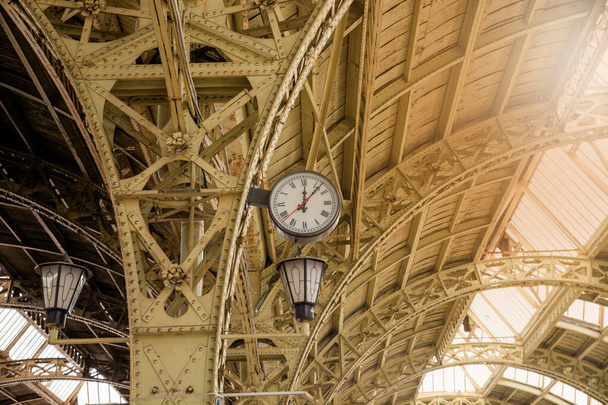Γύρω από το ρωμαϊκό ρολόι και γυάλινη οροφή του σιδηροδρομικού ή του μετρό. Δώδεκα η ώρα, δώδεκα και επτά, ηλιαχτίδα.. - Φωτογραφία, εικόνα