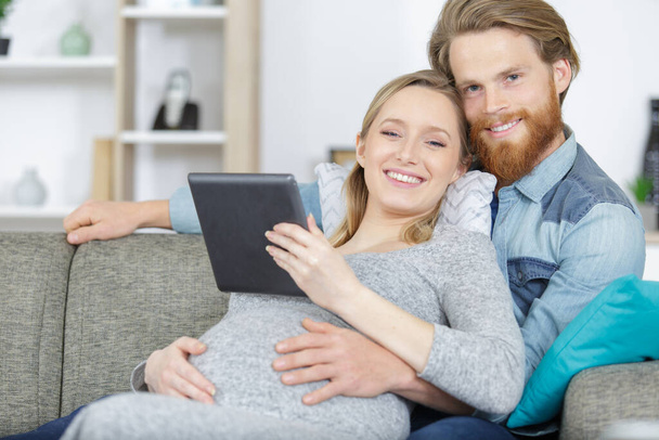 attractive happy young man and pregnant woman holding digital tablet - Fotó, kép