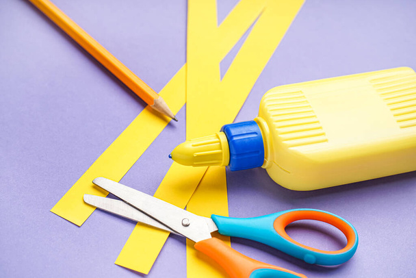 Bottle of glue, paper stripes, pencil and scissors on color background, closeup - Photo, Image