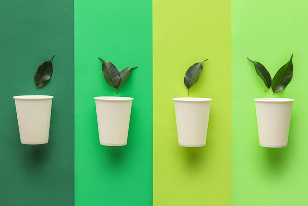 Бумажные чашки с листьями растений на цветном фоне - Фото, изображение