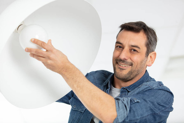 man installing a bulb in living room at home - Foto, afbeelding