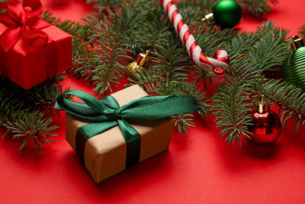 Composition with Christmas gifts and fir branches on red background, closeup - Φωτογραφία, εικόνα