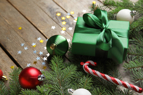 Kompozice s vánočním dárkem, jedlovými větvemi a dekoracemi na dřevěném pozadí, detailní záběr - Fotografie, Obrázek