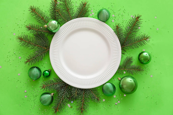 Composición con plato, ramas de abeto y decoraciones navideñas sobre fondo verde - Foto, Imagen