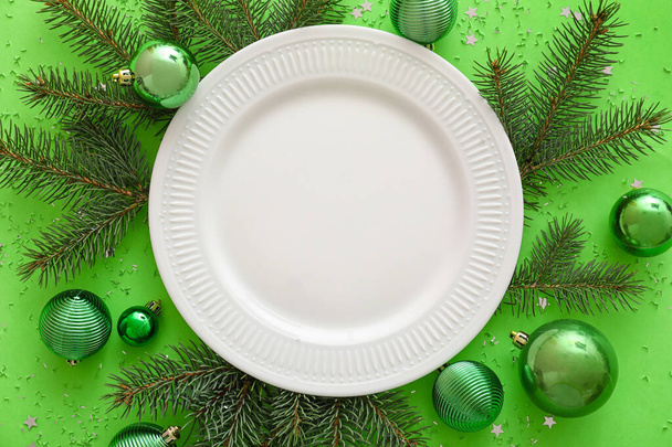 Composition with plate, fir branches and Christmas decorations on green background, closeup - Fotoğraf, Görsel