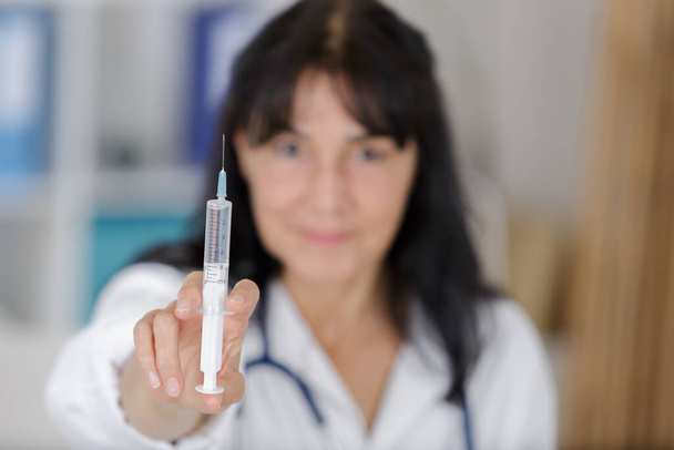 gloved mature doctor in whitecoat holding syringe before making injection - Fotoğraf, Görsel