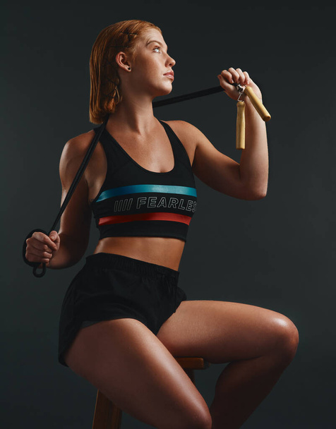 You dont get the butt you want by sitting on it. Studio shot of a sporty young woman posing with a skipping rope against a black background - Foto, Bild