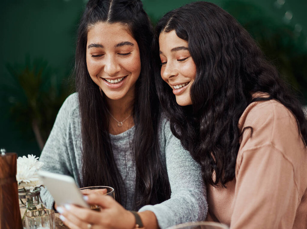La felicidad se duplica cuando la compartimos. hermanas jóvenes usando un smartphone juntas en un café - Foto, imagen